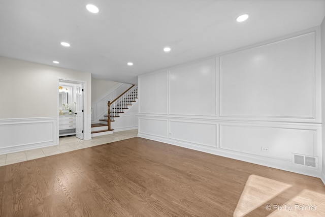 basement with stairway, a decorative wall, visible vents, and light wood-type flooring