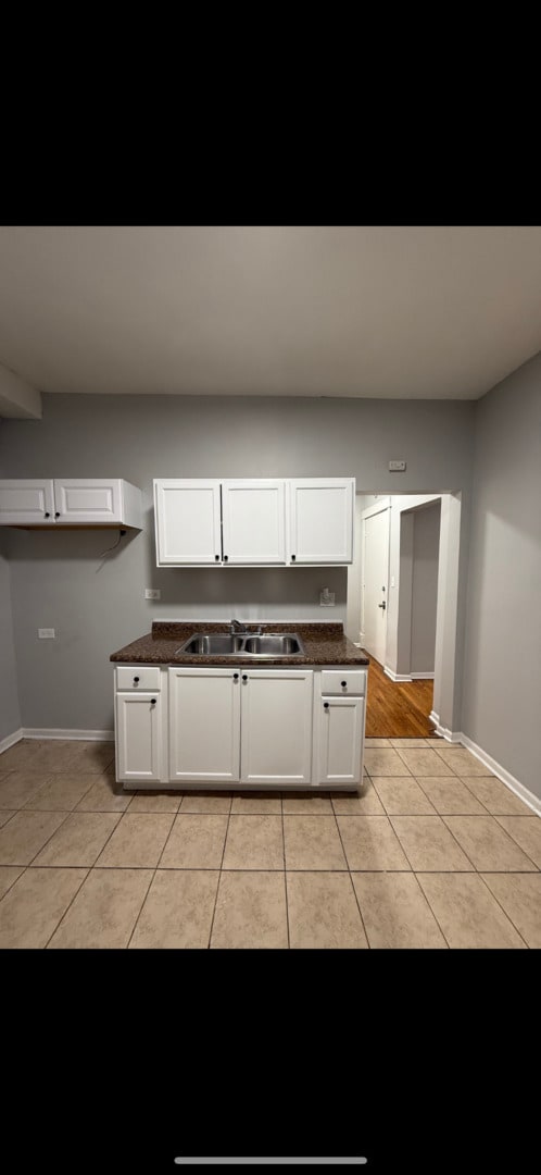 kitchen featuring white cabinetry, dark countertops, light tile patterned flooring, and a sink