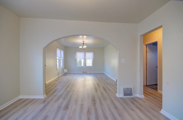 spare room featuring arched walkways, visible vents, baseboards, and light wood-style floors