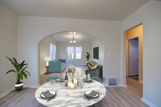 dining area with arched walkways, visible vents, light wood finished floors, and baseboards