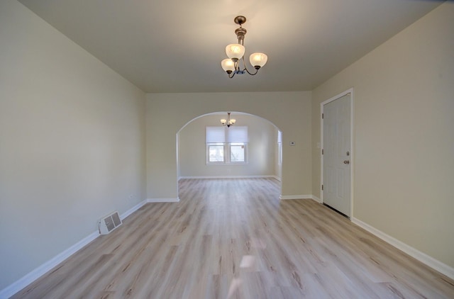 unfurnished room with visible vents, arched walkways, light wood finished floors, baseboards, and a chandelier