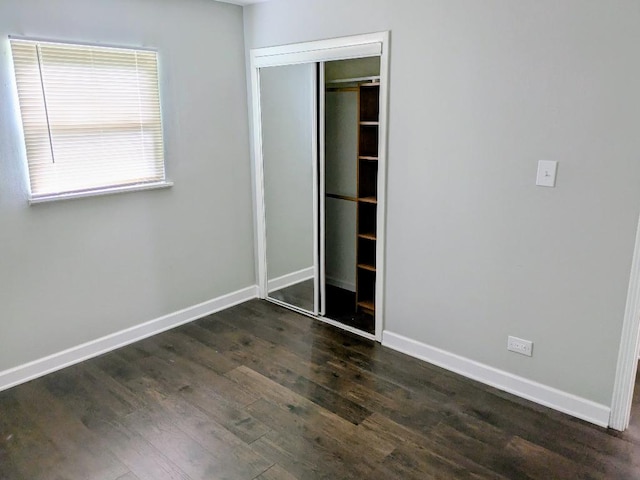 unfurnished bedroom with baseboards, a closet, and dark wood-type flooring