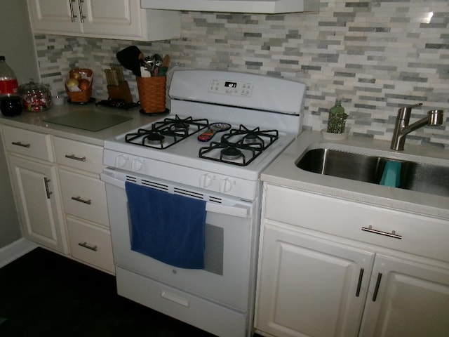 kitchen featuring a sink, decorative backsplash, light countertops, white cabinetry, and white gas range