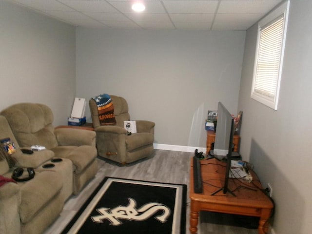 living area with a drop ceiling, baseboards, and wood finished floors