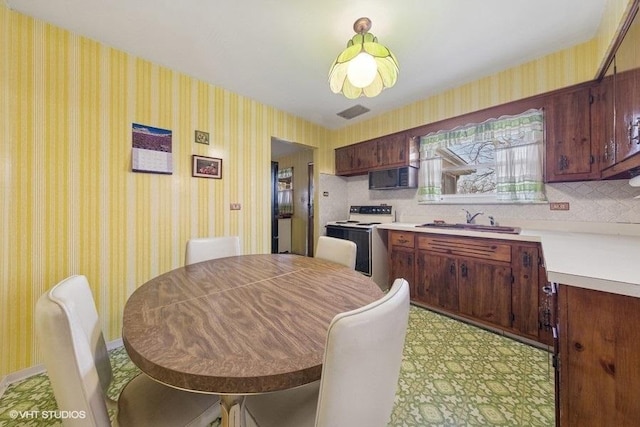 kitchen featuring a sink, wallpapered walls, range with electric stovetop, black microwave, and light countertops