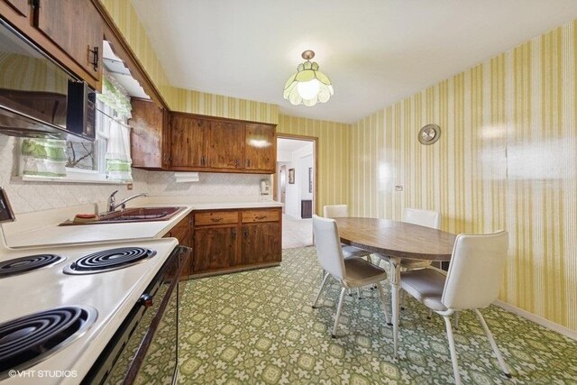 kitchen with wallpapered walls, baseboards, light countertops, electric range, and a sink