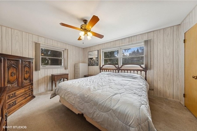 bedroom featuring a ceiling fan, wooden walls, and light colored carpet