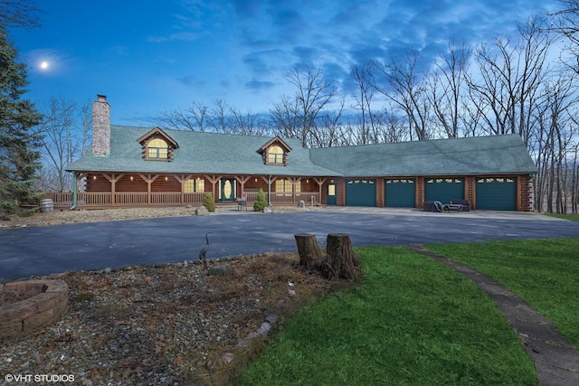 view of front of home featuring a front yard, covered porch, a chimney, a garage, and aphalt driveway