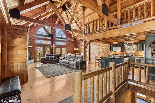 living room with wooden walls, a healthy amount of sunlight, light wood-style floors, and high vaulted ceiling