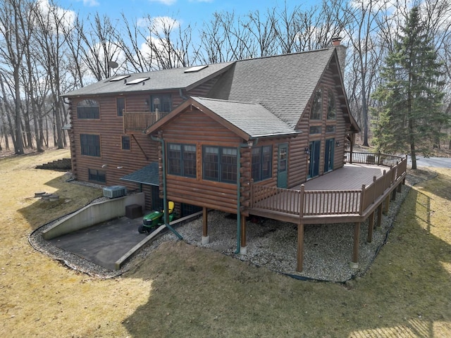 back of house featuring a deck, log exterior, a chimney, and a shingled roof