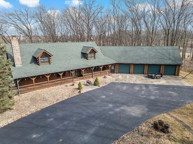 view of front of house featuring aphalt driveway, covered porch, roof with shingles, and a chimney