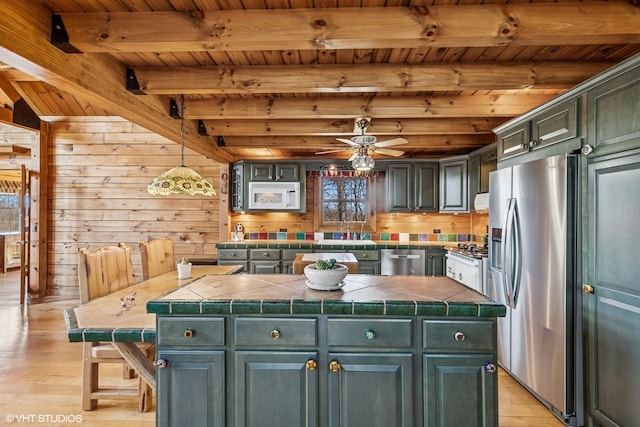 kitchen with light wood finished floors, beamed ceiling, appliances with stainless steel finishes, and a kitchen island