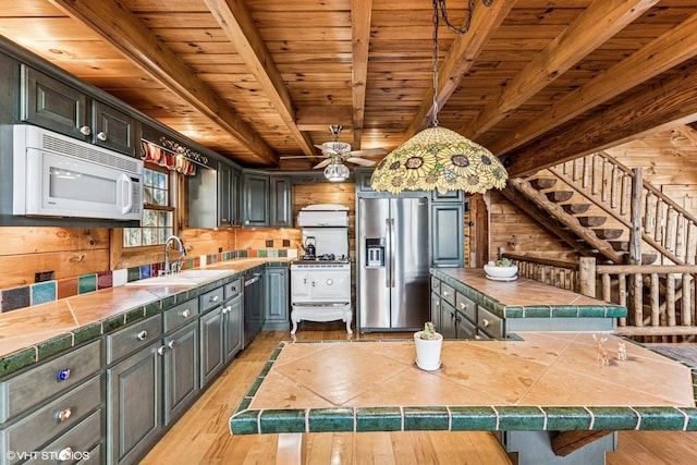 kitchen with beamed ceiling, tile countertops, wooden walls, appliances with stainless steel finishes, and wood ceiling