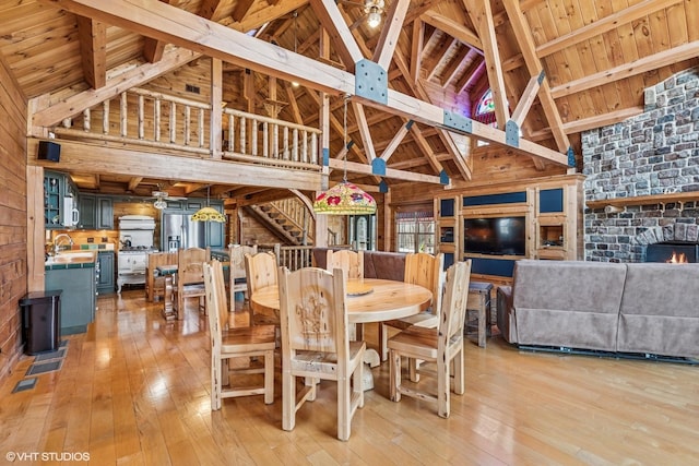 dining space with high vaulted ceiling, stairway, wooden walls, light wood-style floors, and a fireplace