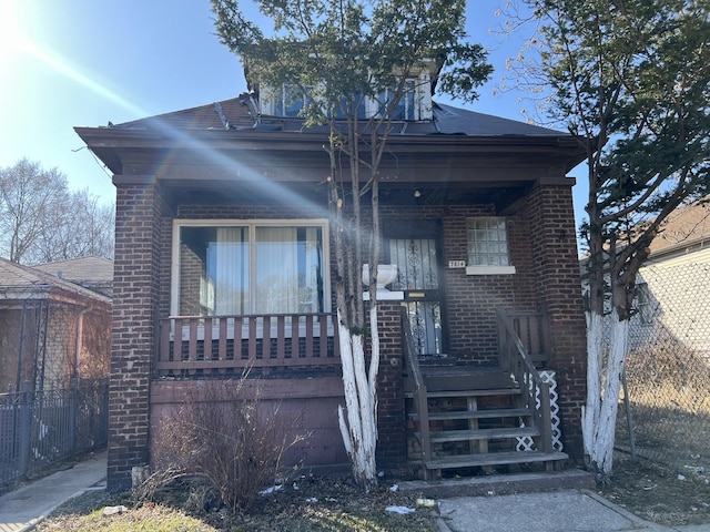 view of front facade with brick siding, a porch, and fence