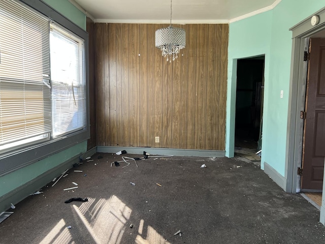 spare room with a chandelier, baseboards, ornamental molding, and wood walls