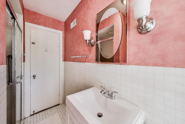 bathroom featuring a wainscoted wall, visible vents, a sink, tile walls, and wallpapered walls