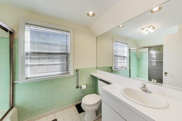 bathroom featuring toilet, vanity, a shower with shower door, tile patterned floors, and tile walls