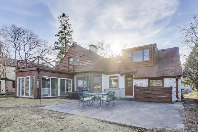 rear view of property with a lawn, a chimney, a patio, and a sunroom