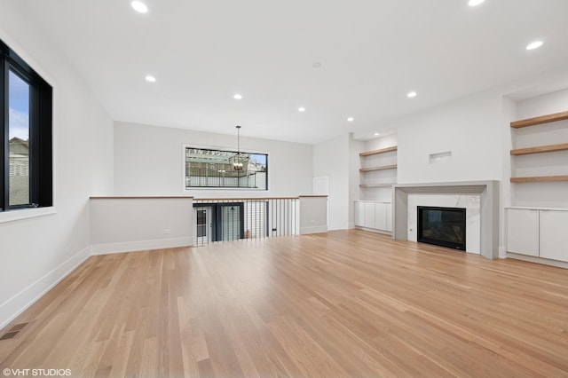 unfurnished living room with built in features, visible vents, baseboards, a premium fireplace, and light wood-style floors