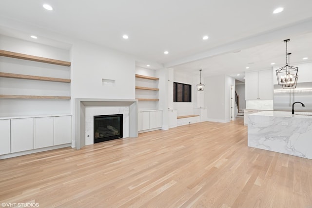 unfurnished living room with light wood-type flooring, built in features, a sink, recessed lighting, and a premium fireplace