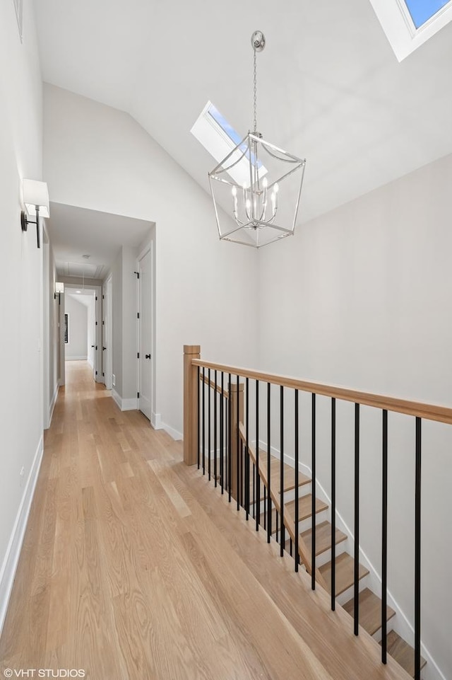 hall featuring lofted ceiling with skylight, an upstairs landing, light wood finished floors, and baseboards