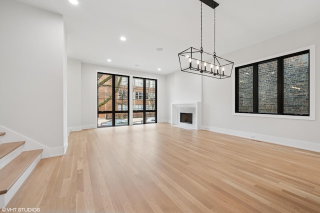 unfurnished living room with light wood-style flooring, recessed lighting, stairway, a premium fireplace, and baseboards