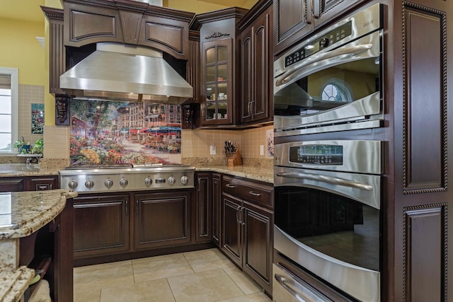 kitchen with light tile patterned flooring, stainless steel appliances, a warming drawer, wall chimney exhaust hood, and backsplash