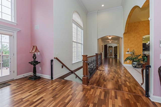 foyer entrance featuring crown molding, wood finished floors, arched walkways, and a towering ceiling