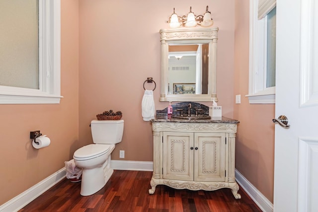 half bathroom featuring vanity, wood finished floors, visible vents, baseboards, and toilet