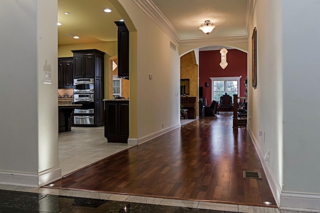 entrance foyer with crown molding, baseboards, arched walkways, and light wood finished floors