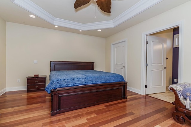 bedroom with a tray ceiling, crown molding, recessed lighting, and wood finished floors