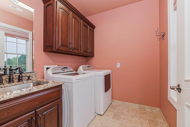 clothes washing area with visible vents, washer and clothes dryer, a sink, cabinet space, and baseboards