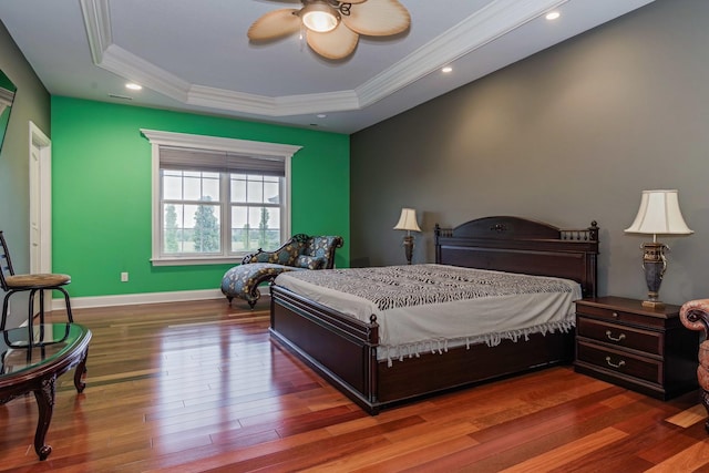 bedroom featuring wood finished floors, baseboards, a tray ceiling, ceiling fan, and crown molding