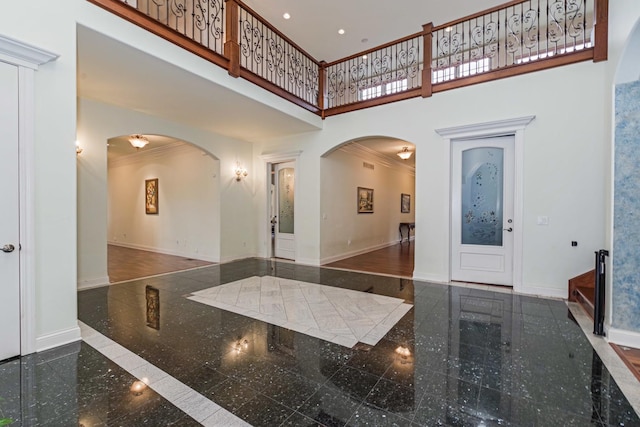 entrance foyer featuring granite finish floor, baseboards, arched walkways, and a towering ceiling