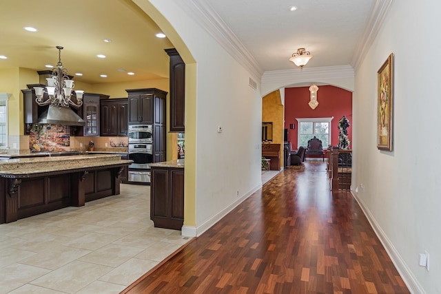 kitchen featuring dark brown cabinets, crown molding, double oven, decorative backsplash, and arched walkways