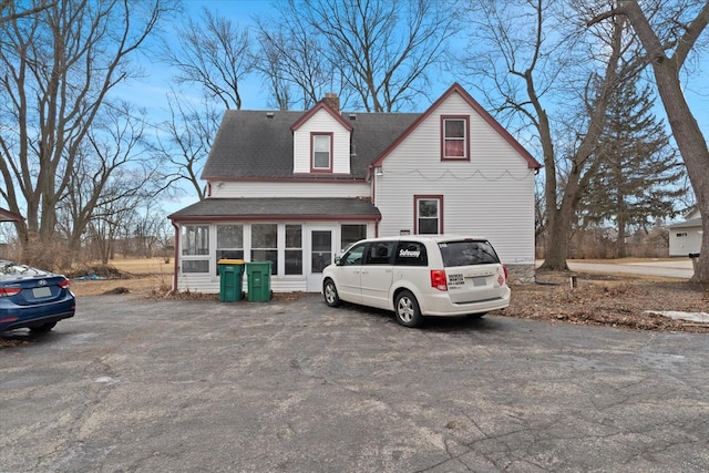 view of front of home featuring a chimney, a sunroom, and roof with shingles