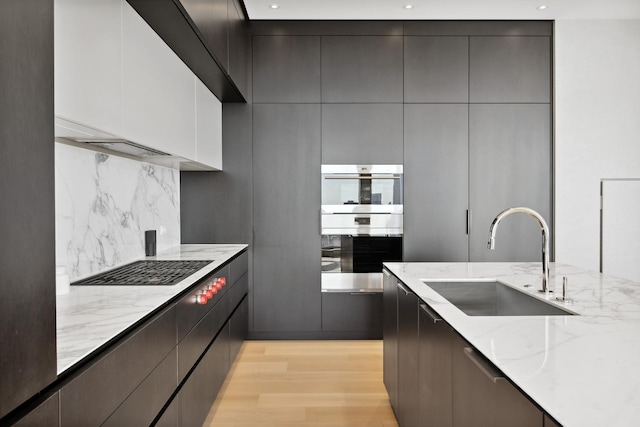 kitchen with light wood-style flooring, double oven, modern cabinets, and a sink