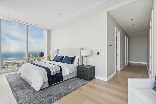 bedroom featuring floor to ceiling windows, light wood-style flooring, baseboards, and a water view