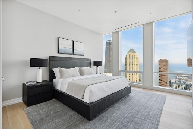 bedroom featuring a wall of windows, baseboards, a city view, and wood finished floors