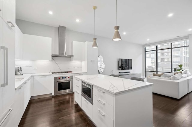 kitchen with a kitchen island, built in microwave, stainless steel oven, wall chimney exhaust hood, and gas cooktop