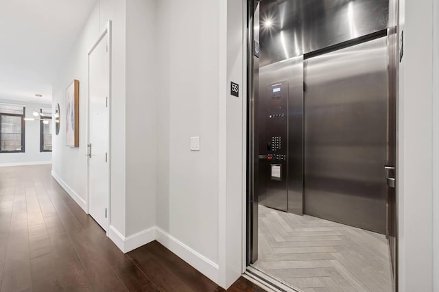 hallway with elevator, parquet flooring, and baseboards