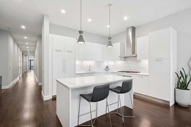 kitchen featuring tasteful backsplash, a center island, wall chimney range hood, dark wood-style flooring, and stainless steel gas cooktop