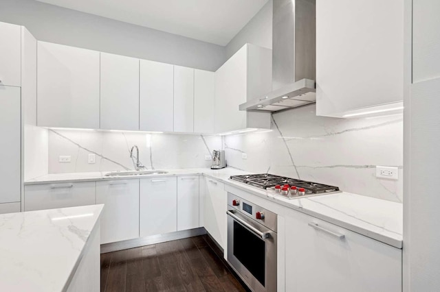 kitchen featuring dark wood-type flooring, wall chimney range hood, appliances with stainless steel finishes, white cabinets, and a sink