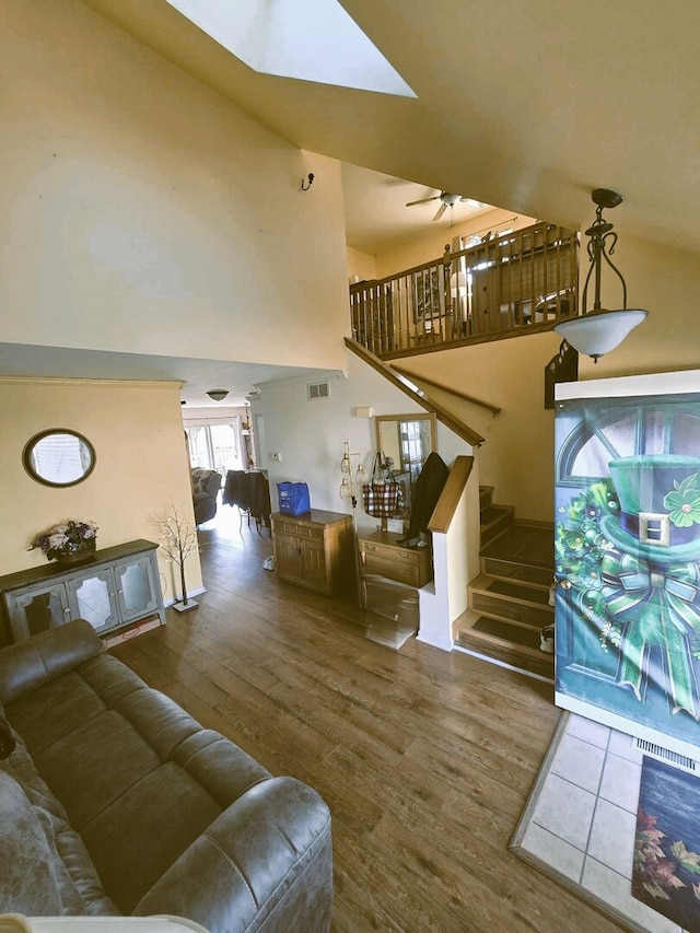 living room with wood finished floors, visible vents, a ceiling fan, a high ceiling, and stairs