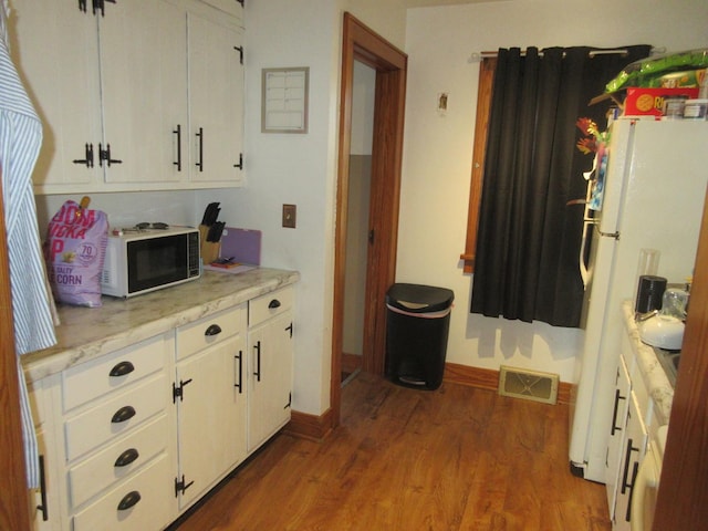 kitchen with visible vents, baseboards, freestanding refrigerator, wood finished floors, and white cabinets