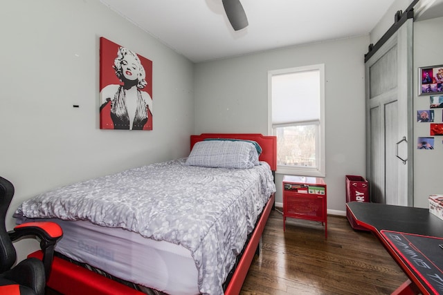 bedroom featuring ceiling fan, baseboards, a barn door, and wood finished floors