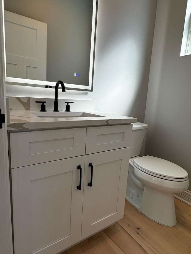 bathroom with toilet, vanity, and wood finished floors