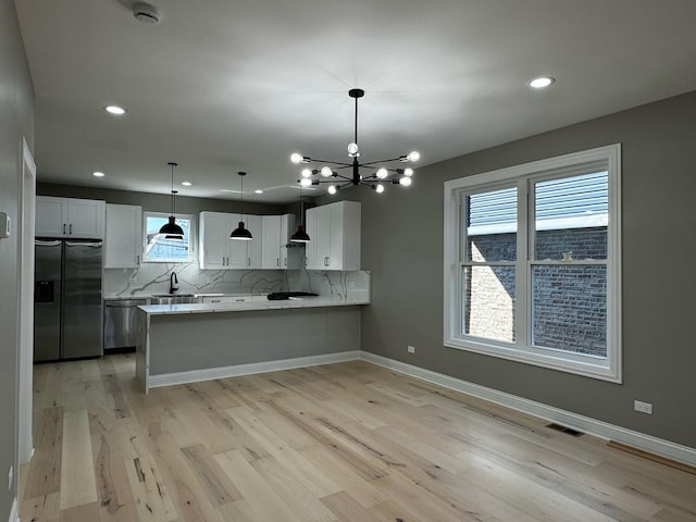 kitchen with backsplash, stainless steel appliances, a peninsula, wall chimney exhaust hood, and light countertops