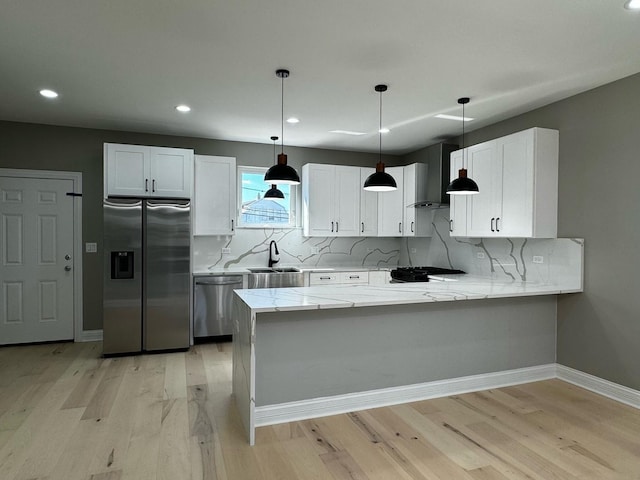 kitchen with a sink, white cabinetry, stainless steel appliances, a peninsula, and wall chimney exhaust hood